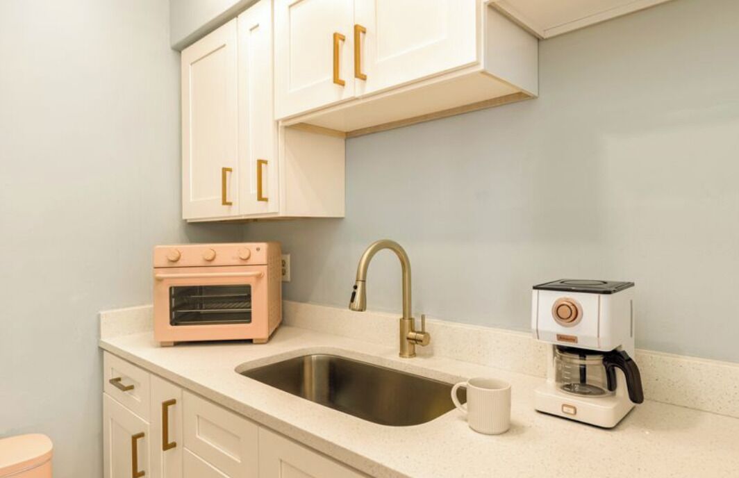 A kitchen with white cabinets, a stainless steel sink, a pink oven, a gold faucet, and a coffee maker.