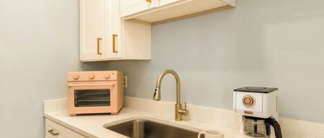 A kitchen with white cabinets, a stainless steel sink, a pink oven, a gold faucet, and a coffee maker.