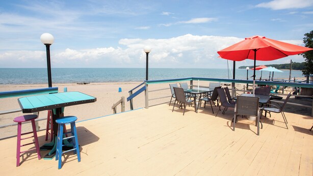 Une terrasse au bord de la plage, avec des tables et des chaises, une piscine et une vue sur l’océan.