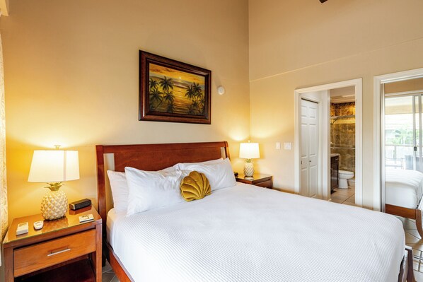 Une chambre d’hôtel avec un grand lit, deux tables de chevet avec des lampes, un tableau encadré au mur et une porte donnant accès à une salle de bain.