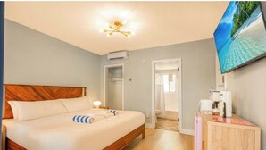 A hotel room with a wooden bed, a flat-screen TV mounted on the wall, and a wooden cabinet with toiletries. - 3 min to beach ~ pool ~ free parking ~ (Clearwater)
