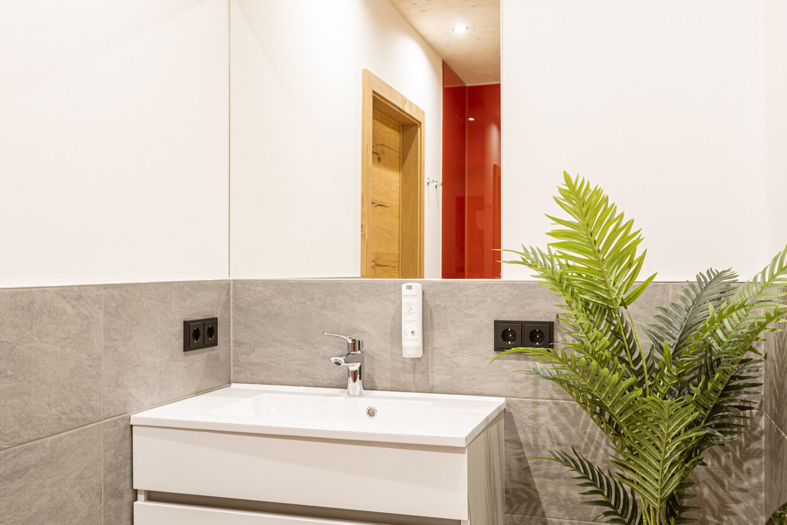 Un baño moderno con un lavamanos blanco, un espejo y una planta en maceta.