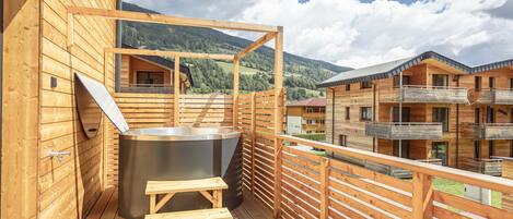 A wooden balcony with a hot tub, wooden railings, and a view of a mountainous landscape.
