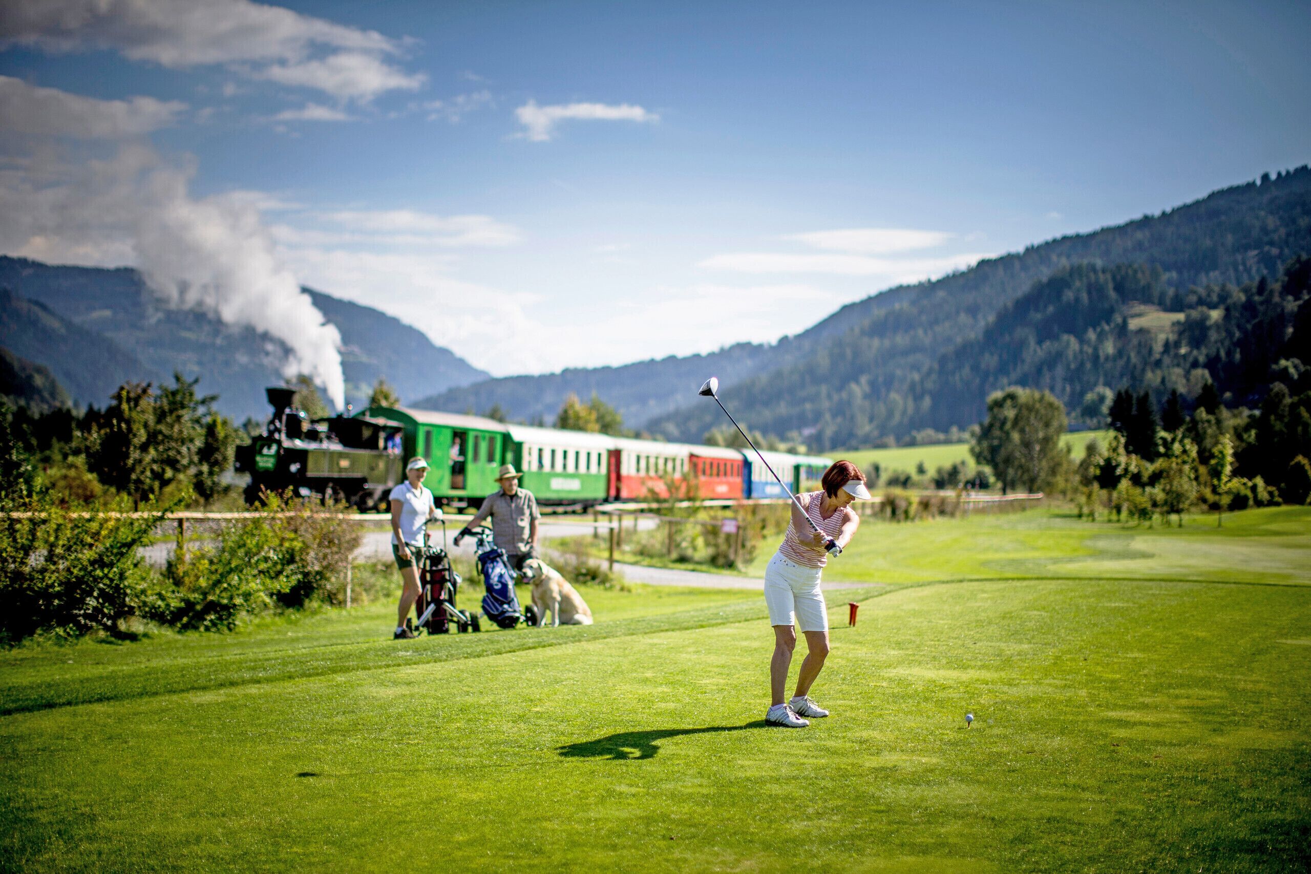 Un campo de golf con un tren al fondo y montañas.
