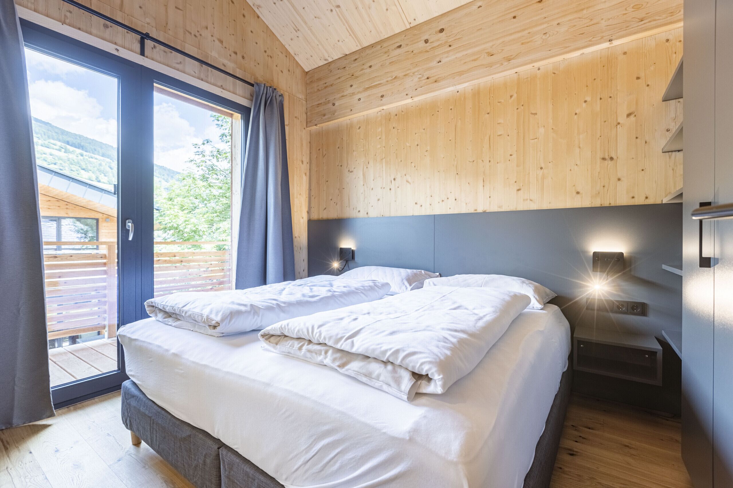 Un dormitorio con una cama grande, techo de madera y vistas a una terraza exterior por medio de una puerta corrediza.
