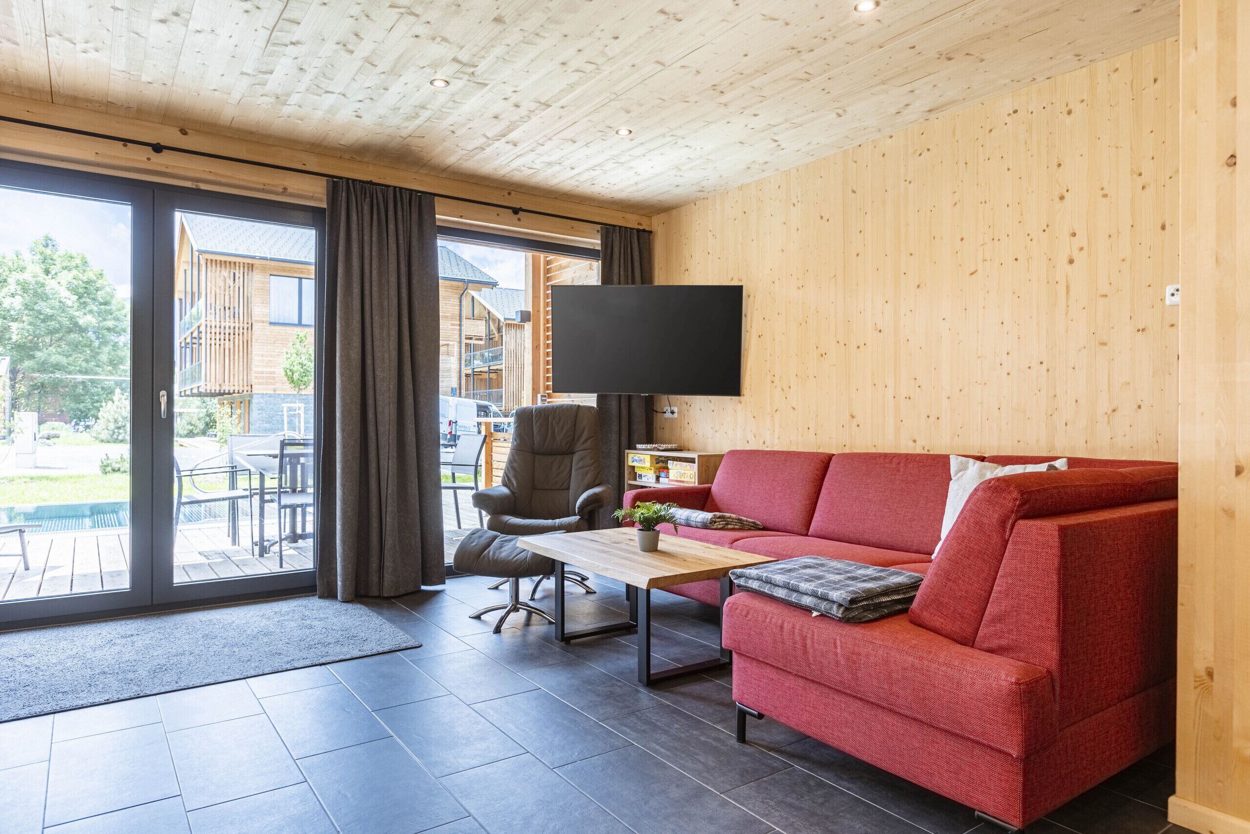 Una sala de estar moderna con un sofá rojo, una mesa de centro de madera y un televisor de pantalla plana montado en la pared.