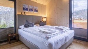 Ein modernes Schlafzimmer mit einem großen Bett, Holzwänden und Blick auf eine verschneite Landschaft.