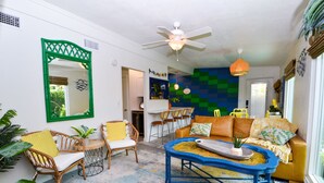 A living room with a ceiling fan, a coffee table, and a sofa. There is a mirror on the wall and a plant on the floor.