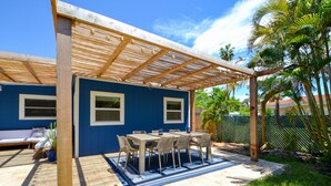 A covered patio with a table and chairs, a wooden pergola, and a blue wall.