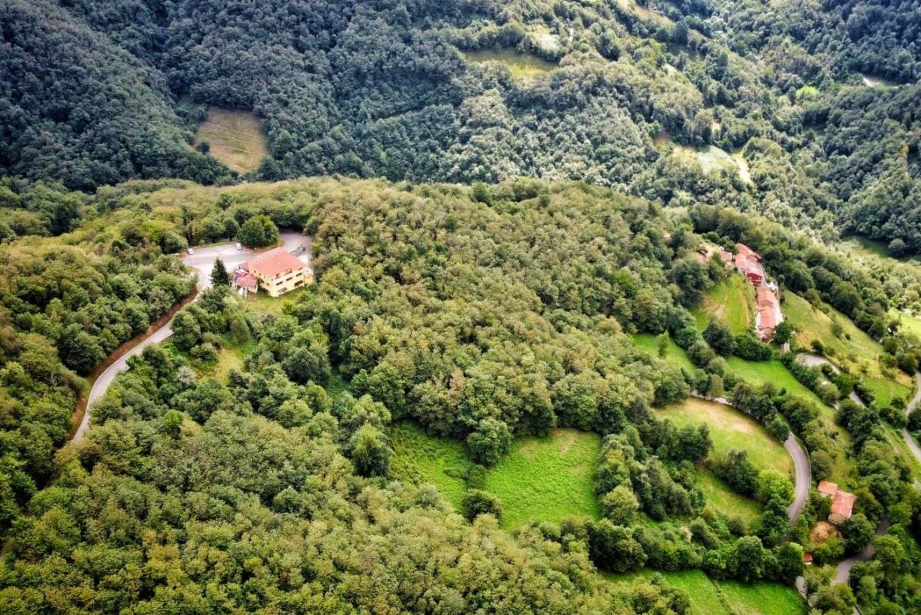 Luchtbeeld van een bebost gebied met een gebouw met rood dak, omgeven door groen en slingerende paden.