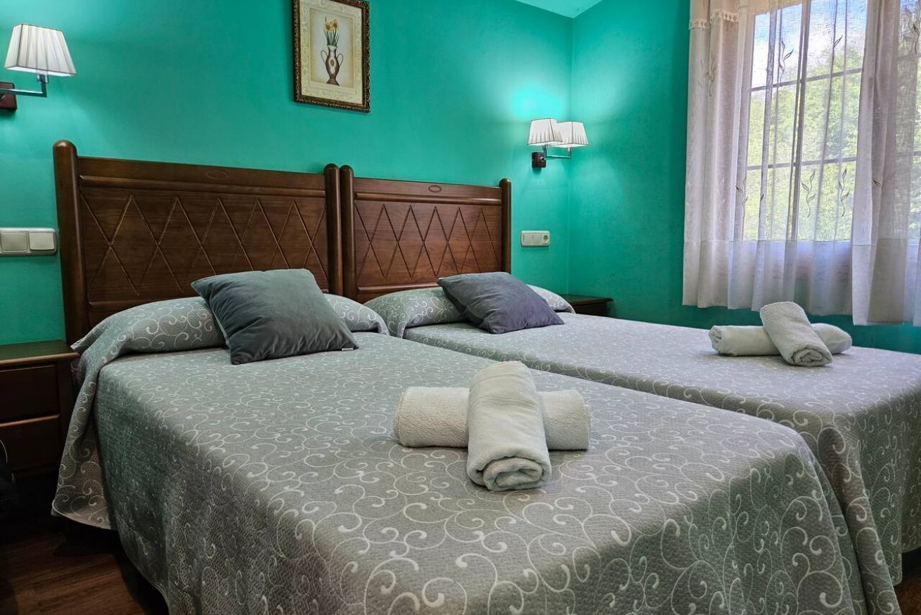 A hotel room with two beds, teal walls, and a window with curtains.