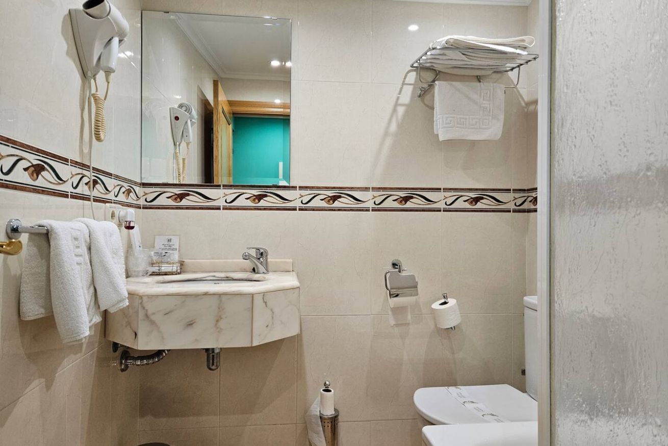 A bathroom with a marble sink, a hairdryer, a toilet, and a towel rack.