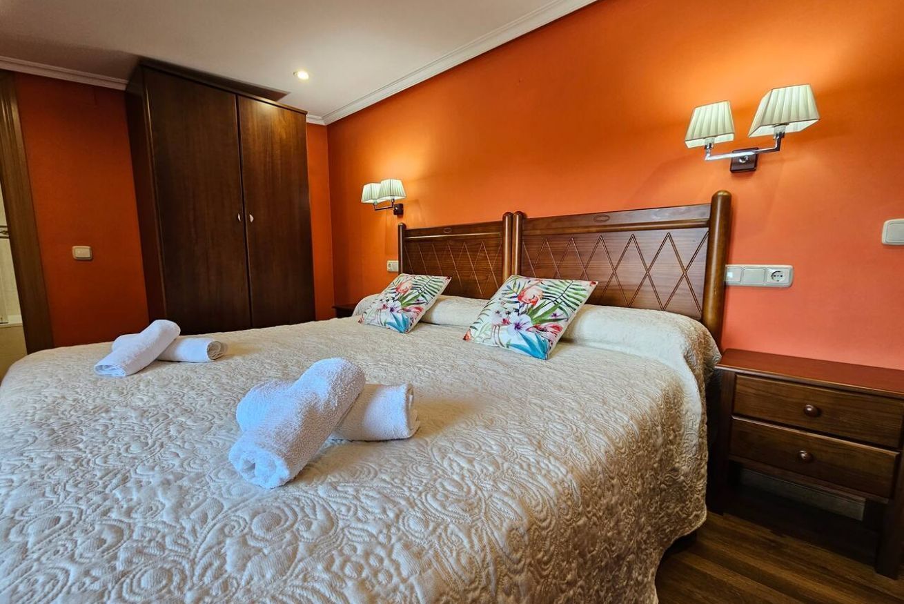 Una habitación de hotel con una cama grande, dos lámparas de noche, un armario de madera y una mesita de noche.