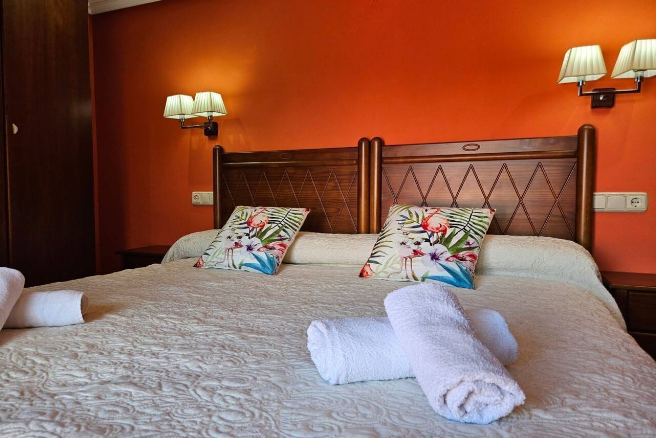 A hotel room with a wooden headboard, floral pillows, a bed with a textured blanket, and two wall-mounted lamps.