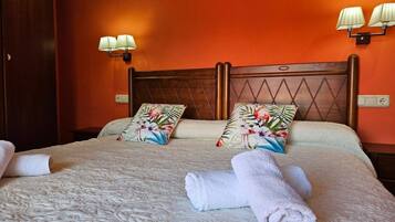 A hotel room with a wooden headboard, floral pillows, a bed with a textured blanket, and two wall-mounted lamps.