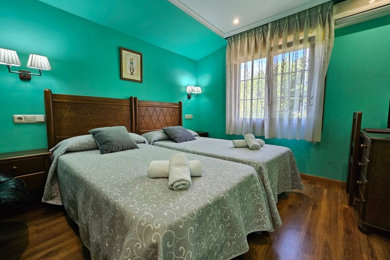 Habitación con dos camas, cabecero de madera, ventana con cortinas, lámparas de pared e imagen en un marco.