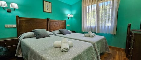A room with two beds, a wooden headboard, a window with curtains, wall-mounted lamps, and a framed picture.