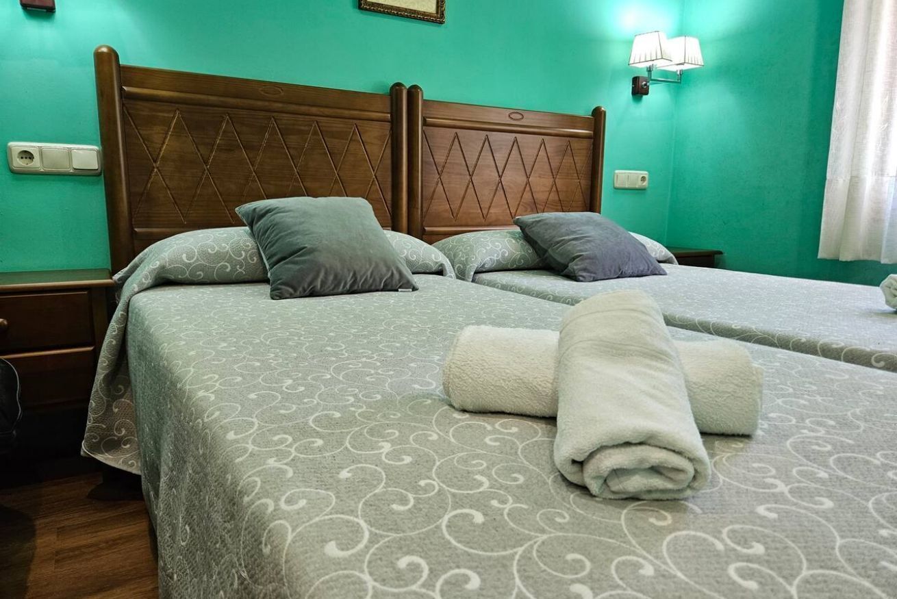 Een tweepersoonsbed met een beddegoed met patroon, twee kussens en een opgerolde handdoek.
