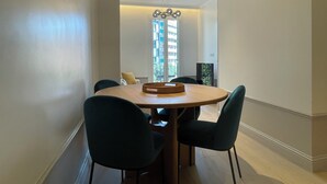 A dining area with a round wooden table, four dark green chairs, and a woven basket on the table. - Apartment Luxury one bed one Bathroom (Barcelona)