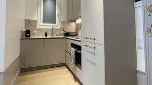 A compact kitchen with white cabinets, a marble backsplash, a built-in oven, and a small window above the sink. - Apartment Luxury one bed one Bathroom (Barcelona)