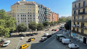 A multi-story building with a mix of residential and commercial spaces, a clear road with vehicles, and trees lining the street. - Apartment Luxury one bed one Bathroom (Barcelona)