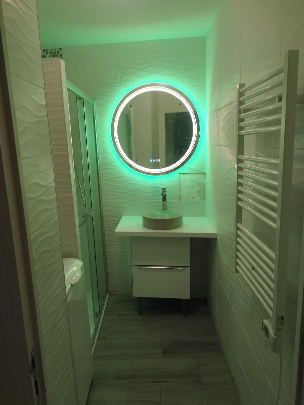 A narrow bathroom with a round mirror, a sink, and a towel rack.