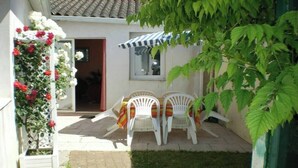 A patio with white plastic chairs and a striped awning, a white lattice with flowers, and a green-leaved tree.