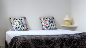 A bedroom with a bed, two patterned pillows, a bedside lamp, and a tiled floor.