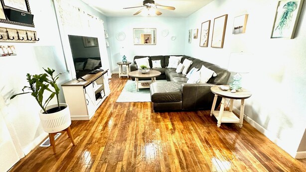 A living room with a dark leather sofa, wooden flooring, a ceiling fan, and various framed pictures on the walls.
