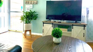 A living room with a wooden coffee table, a television on a wooden stand, a potted plant, and a sign on the wall.