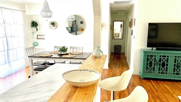 A modern living room with a wooden dining table, white chairs, a large bowl, and a green cabinet with a TV. - Cozy Ranch Home, Centrally Located near Chicks Beach! (Virginia Beach)