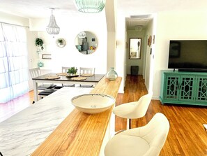 A modern living room with a wooden dining table, white chairs, a large bowl, and a green cabinet with a TV. - Cozy Ranch Home, Centrally Located near Chicks Beach! (Virginia Beach)