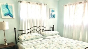 A bedroom with a bed, pillows, a nightstand, a lamp, and curtains. - Cozy Ranch Home, Centrally Located near Chicks Beach! (Virginia Beach)