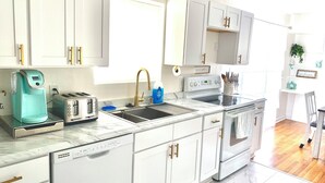 A modern kitchen with white cabinets, a built-in oven, a dishwasher, and a coffee maker. - Cozy Ranch Home, Centrally Located near Chicks Beach! (Virginia Beach)