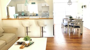 A spacious living area with a kitchen in the background, wooden flooring, and a dining area with a chandelier. - Cozy Ranch Home, Centrally Located near Chicks Beach! (Virginia Beach)