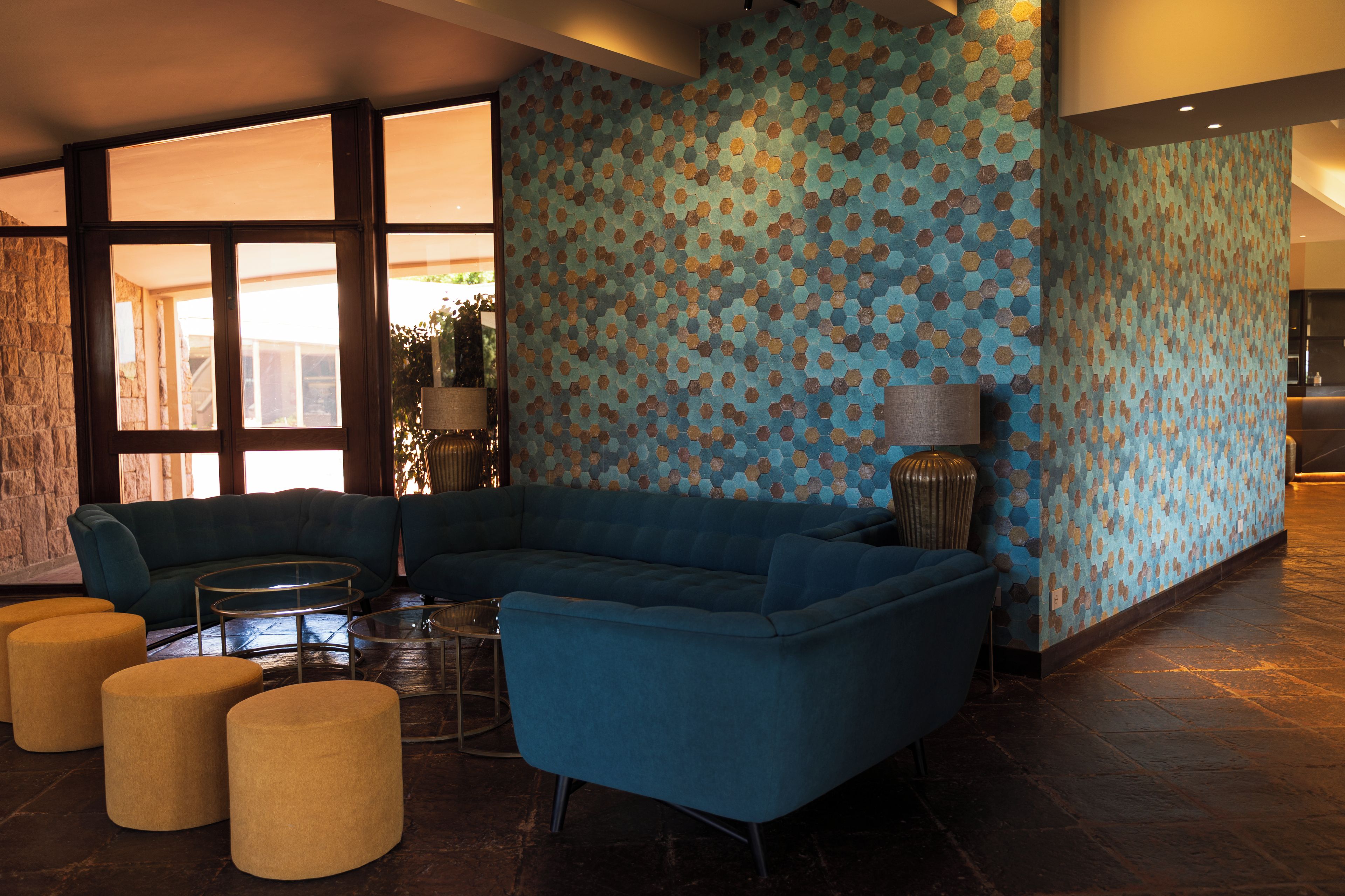 A modern lounge area with a blue sectional sofa, a glass coffee table, and two round ottomans.