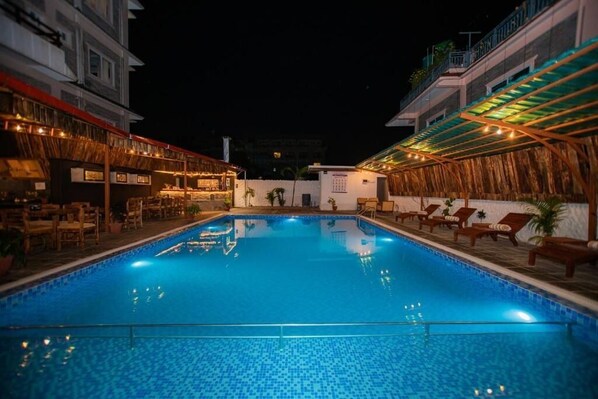 A swimming pool with lounge chairs and a bar area, surrounded by buildings. - Majheri Resort and Spa (Pokhara)