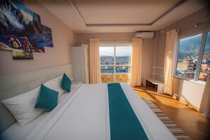 A hotel room with a large bed, a view of the city, and a painting on the wall. - Majheri Resort and Spa (Pokhara)