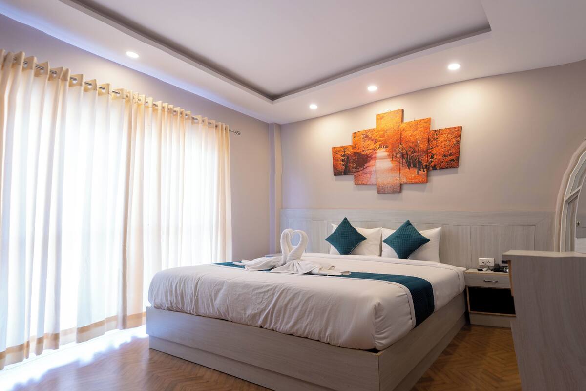 Ein modernes Hotelzimmer mit einem großen Bett, einem Nachttisch, einem Wandbild und einem Fenster mit Vorhängen.