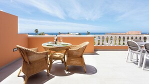 A balcony with wicker furniture, a table set with plates and glasses, and a view of the sea. - Exclusive Penthouse close to the beach, heated pool, aircondition, dishwasher (Playa de la Américas)