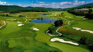 Campo de golfe com bunkers de areia, obstáculos de água e um clube de campo ao fundo.