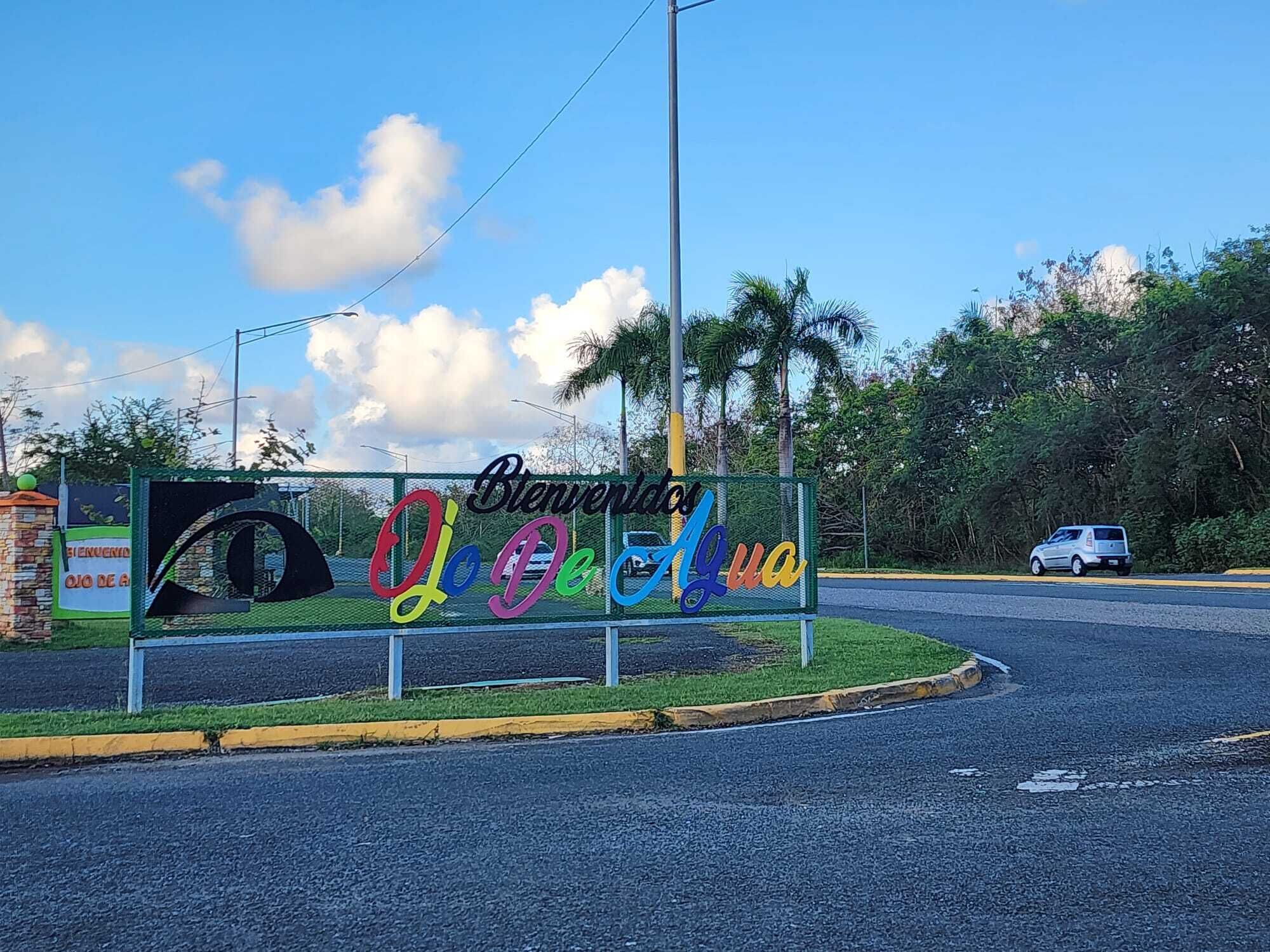 A welcome sign with colorful letters and a road with a car and a truck.