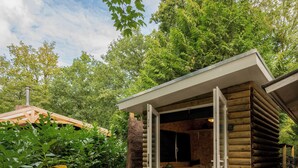 A wooden cabin with a glass door, a small patio with a chair, and a tiled floor.