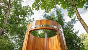 A wooden outdoor shower with a metal frame, surrounded by lush greenery and trees.