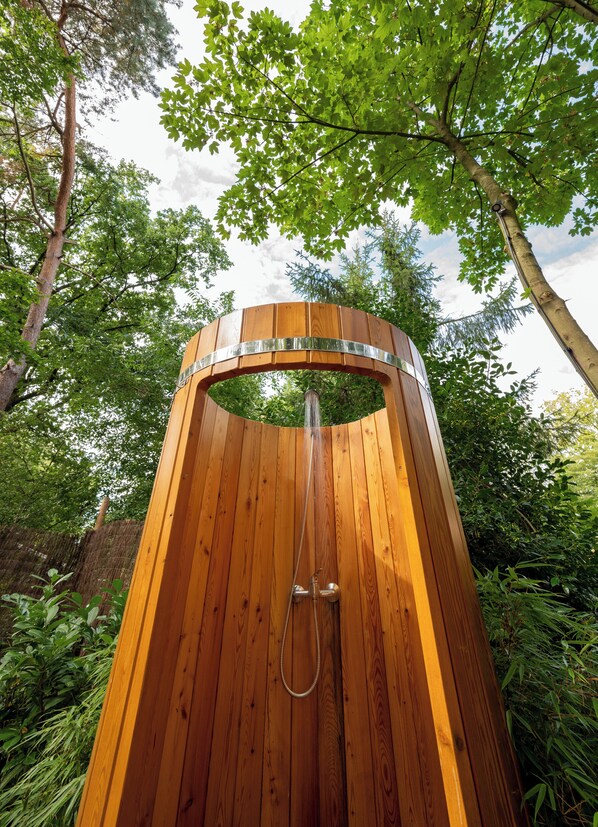 A wooden outdoor shower with a metal frame, surrounded by lush greenery and trees.