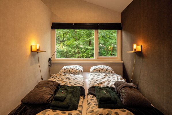 A room with two beds, a window with a view of greenery, and wall-mounted lights. - ZEN-Bungalow no 4 with sauna and hottub (Rheezerveen)