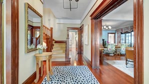 A spacious hallway with wooden flooring, a staircase, and a dining area with floral upholstery. - Sonoma Victorian in Heart of Sonoma (Sonoma)