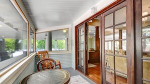 A covered porch with a wooden table and chairs, large windows, and a sliding glass door leading to an interior space. - Sonoma Victorian in Heart of Sonoma (Sonoma)