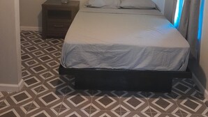 A bedroom with a bed, nightstand, and patterned floor.