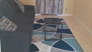 A living room with a dark sofa, patterned cushions, a small table, and a patterned rug.